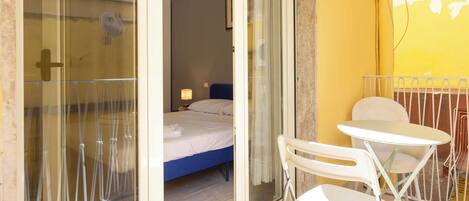 A room with a bed, a small table, and chairs, a glass door, and a yellow wall.