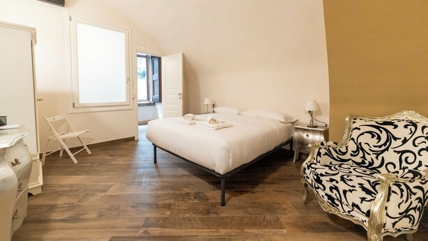 Un dormitorio con cama, mesitas de noche, una silla y una ventana.