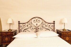 Een bed met een decoratief metalen hoofdbord, twee nachtkastjes met lampen, en een effen muur.