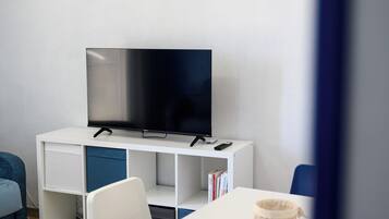 Una camera moderna con una TV a schermo piatto su un mobile bianco, una scrivania bianca con una sedia e una poltrona blu.