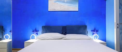 A bedroom with a bed, white bedding, a painting of a beach scene, and star-shaped night lights on nightstands.