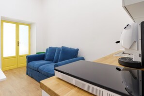 Een kamer met een blauwe bank, een witte koffieapparaat en een houten tafel.