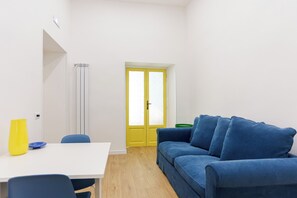 A room with a white table, blue chairs, a blue sofa, a yellow door, and a green trash bin. - Santa Patrizia a Chiaia Apartment  (Naples)