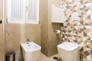 Ein Badezimmer mit integriertem Bidet, Toilette und einem Fenster mit Vorhängen.