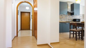 Un couloir mène à une cuisine dotée d’une porte en bois, d’une table à manger avec des chaises et d’un four à micro-ondes posé sur le comptoir.