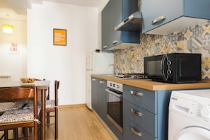 A compact kitchen with a microwave, oven, and washing machine, wooden dining table, chairs, and patterned backsplash. - Domus Angelina (Rome)
