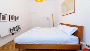A neatly made bed with white linens, a wooden headboard, and a map on the wall. - Boho 202 (Rome)
