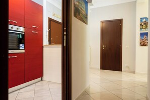 Een moderne keuken met rode kastjes, een ingebouwde oven en een houten deur naar een andere kamer.