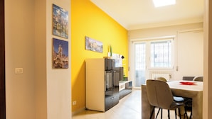 Una cocina moderna con una pared de acento amarilla, un refrigerador y un comedor con sillas.