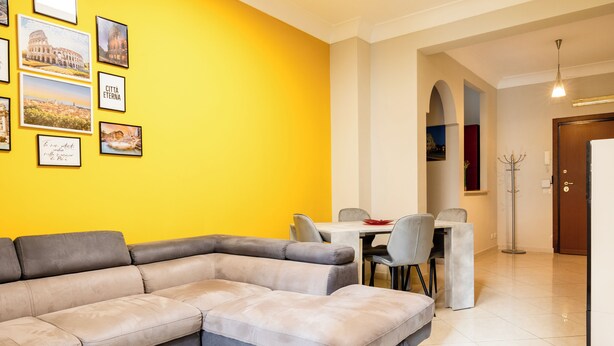 Ein modernes Wohnzimmer mit einem Ecksofa, einem Esstisch mit Stühlen und gerahmten Bildern an der Wand.