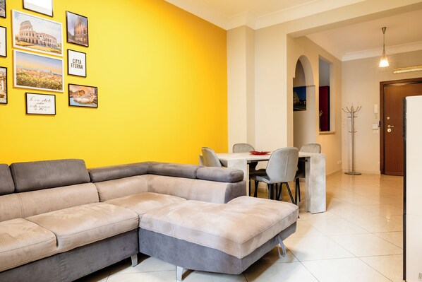 Een moderne woonkamer met een modulaire bank, een eettafel met stoelen en kunstwerken in lijsten aan de muur.
