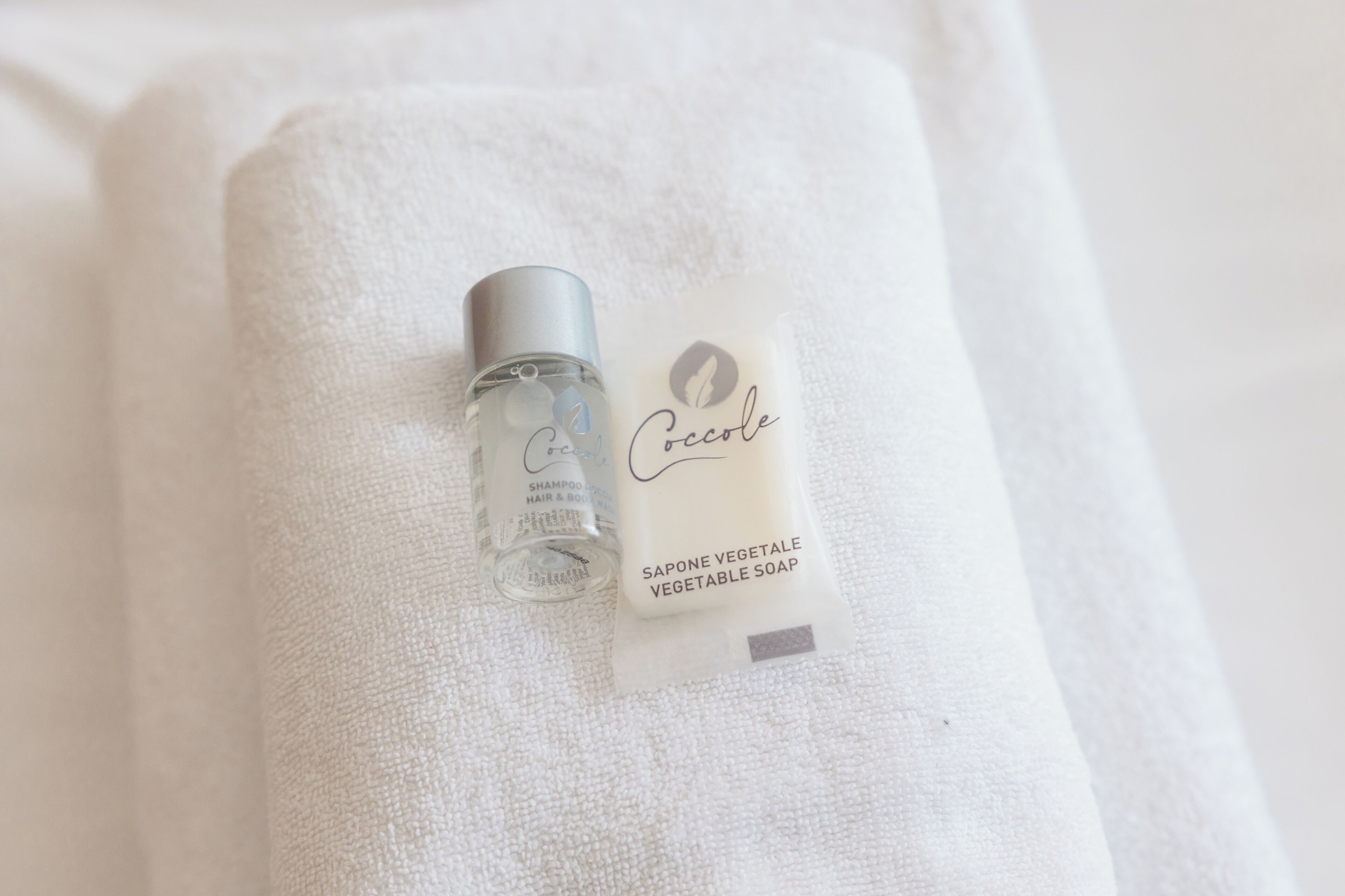 Una bottiglia trasparente di shampoo e una confezione di sapone vegetale su un asciugamano bianco.