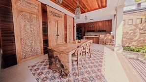 Eine moderne Küche mit Holzschränken, einem Essbereich mit großem Tisch und Stühlen sowie einer hängenden Leuchte.
