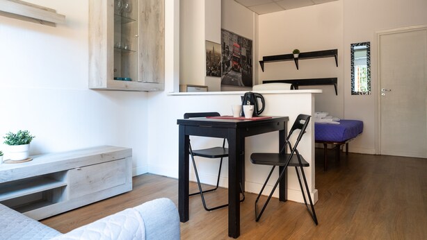 Ein modernes Wohnzimmer mit Esstisch, Stühlen, einer Kaffeemaschine und einem blauen Sofa.