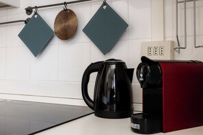 Eine Küche mit einem schwarzen Wasserkocher, einer roten Kaffeemaschine und zwei grünen Küchentüchern, die an der Wand hängen.