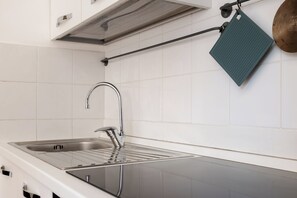 A kitchen with a stainless steel sink, a black countertop, and a hanging green towel. - Montagnola Mini House (Rome)