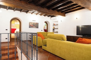 Ein Wohnzimmer mit einem gelben Sofa, einem Fernseher und einer Treppe mit Geländer.