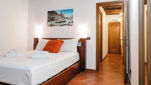 Une chambre d’hôtel avec un lit, une tête de lit en bois, un tableau représentant un paysage urbain et une porte donnant sur une autre pièce.