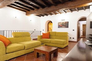 Ein Wohnzimmer mit zwei Sofas, einem Couchtisch und einem Fernseher. Die Decke ziert sich mit Holzbalken, und an der Wand hängt ein Gemälde.