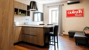 A modern kitchen with wooden cabinets, a black pendant light, and a dining area with a black sofa and a table.