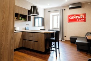 Eine moderne Küche mit Holzausstattung, einer schwarzen Pendelleuchte und einem Essbereich mit schwarzem Sofa und Tisch.