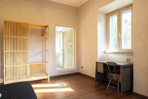 Ein Zimmer mit Holzschrank, Schreibtisch mit Stuhl, Fenster und einer Dusche.