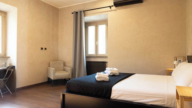 A modern hotel room with a large bed, a chair, a desk, and a window with curtains.