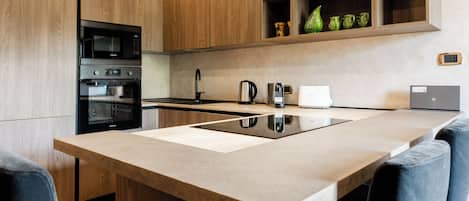 A modern kitchen with wooden cabinets, a built-in oven, a microwave, and a large island with a sink.