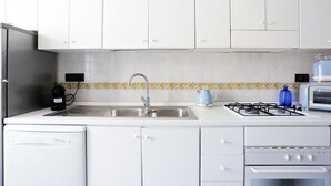 Ett kök med vita skåp, en diskho i rostfritt stål, en gasspis, en brödrost och en diskmaskin.