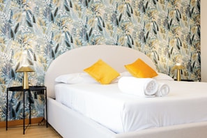 A neatly made bed with white linens and two yellow pillows, a bedside lamp, and a wall with a leaf pattern. - Riviera di Chiaia 207 - 7° Piano (Naples)