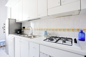 A kitchen with white cabinets, a gas stove, a sink, and a kettle. - Riviera di Chiaia 207 - 7° Piano (Naples)