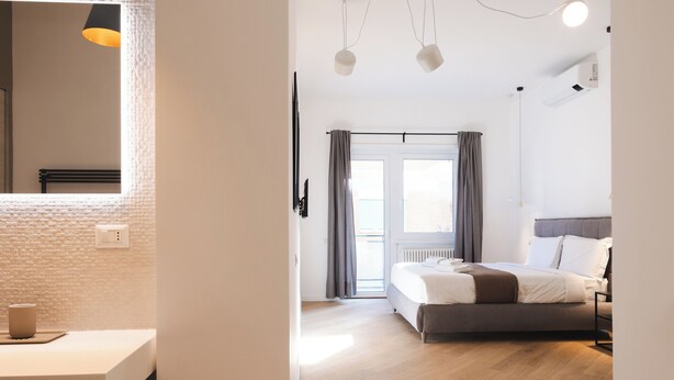 A modern bedroom with a bed, bedside table, and a view of the outdoors through a window. - Domus Solis (Rome)