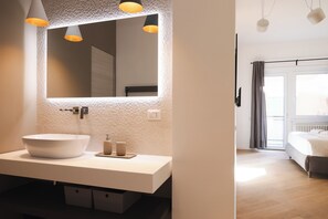 Un baño moderno con un espejo grande, lavamanos blanco e iluminación colgante.