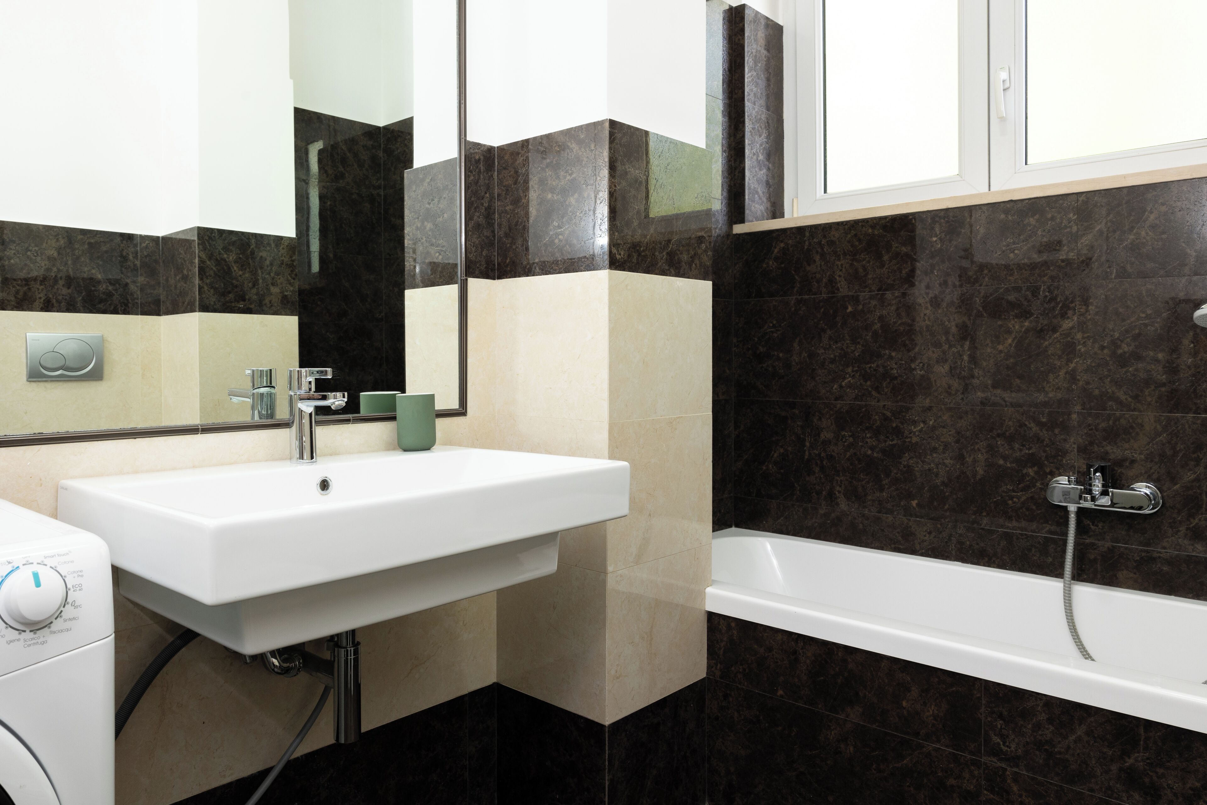 A bathroom with a white sink, a mirror, a green cup, a white toilet, and a bathtub with a showerhead.