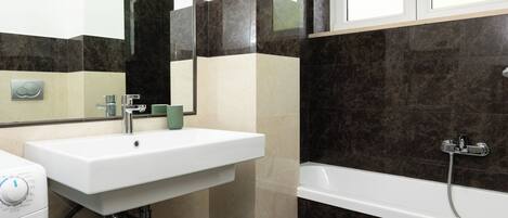 A bathroom with a white sink, a mirror, a green cup, a white toilet, and a bathtub with a showerhead.
