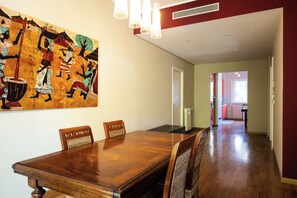 Un comedor con una mesa y sillas de madera, un cuadro decorativo grande en la pared y un pasillo que conduce a otras habitaciones.