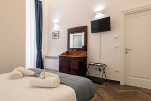 A hotel room with a bed, a wooden dresser, a mirror, a television, and a door. - Palazzo Guida al Duomo (Naples)