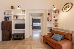 A living room with a brown leather sofa, a television, and bookshelves filled with books and decorative items. - Palazzo Guida al Duomo (Naples)