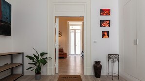 Ein Flur mit Holzboden, einer Fußmatte, einem Blumentopf, einem Metalltisch und Wandbildern.