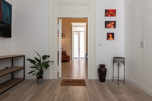 Ein Flur mit Holzboden, einer Fußmatte, einem Blumentopf, einem Metalltisch und Wandbildern.
