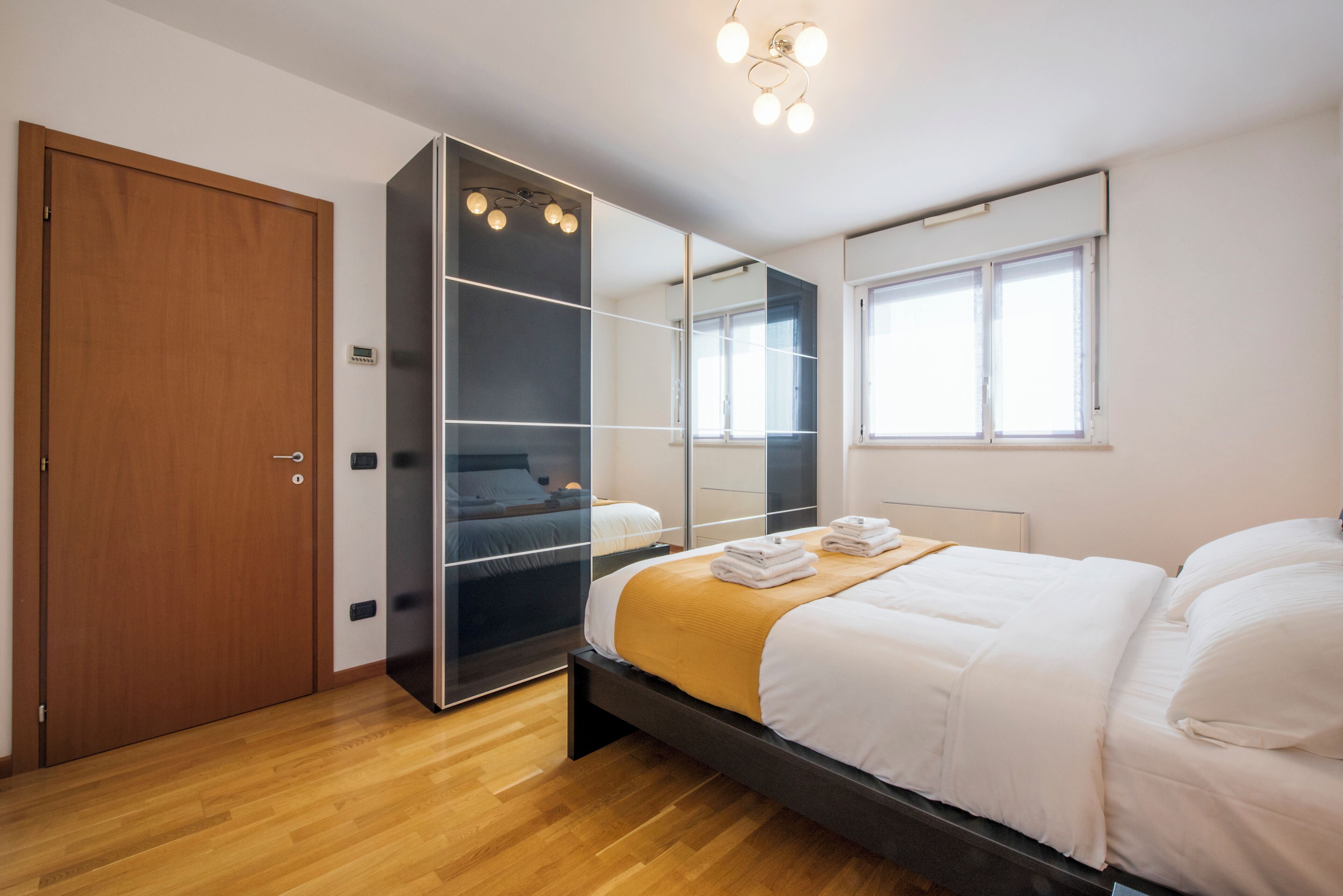 A bedroom with a bed, a wardrobe, a mirror, and a window.
