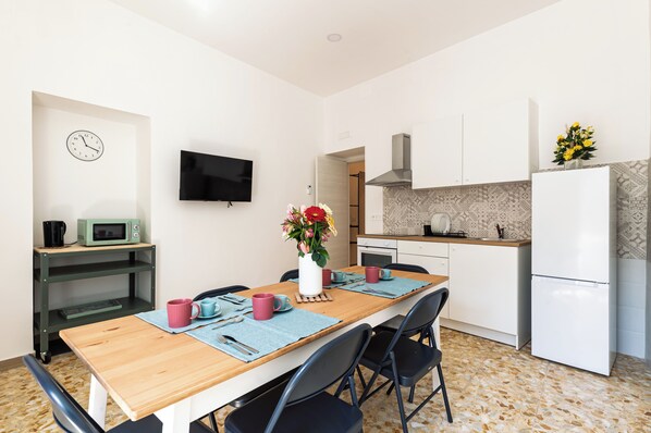 A modern kitchen with a microwave, stove, and refrigerator. There is a dining table with chairs and a TV mounted on the wall. - Casa Luce del Sole (Naples)