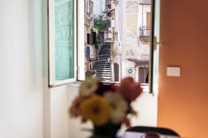 A narrow street view through a window with a flower arrangement on a table. - Casa Luce del Sole (Naples)