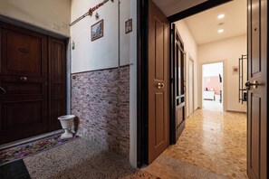 A hallway with a stone wall, wooden doors, and a tiled floor. - Casa Luce del Sole (Naples)