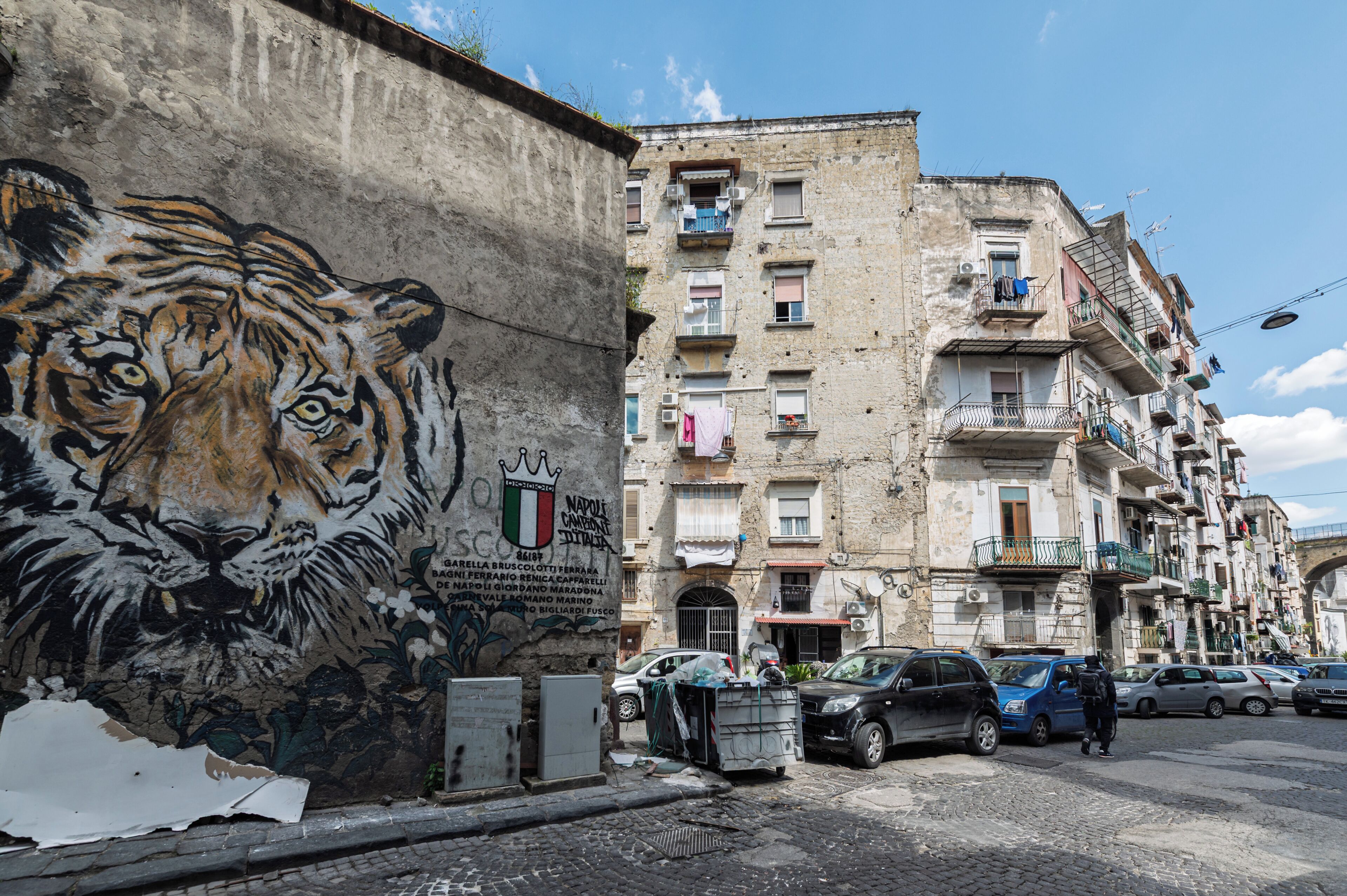 Ein Gebäude mit Wandgemälde eines Tigers, Balkonen mit Wäsche und geparkten Autos.