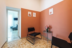 A room with a black chair, a small table with a vase, and a sofa in the background. - Casa Luce del Sole (Naples)