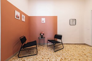 Ein Zimmer mit zwei schwarzen Stühlen, einem kleinen Tisch mit Blumenvase und Bildern an den Wänden.