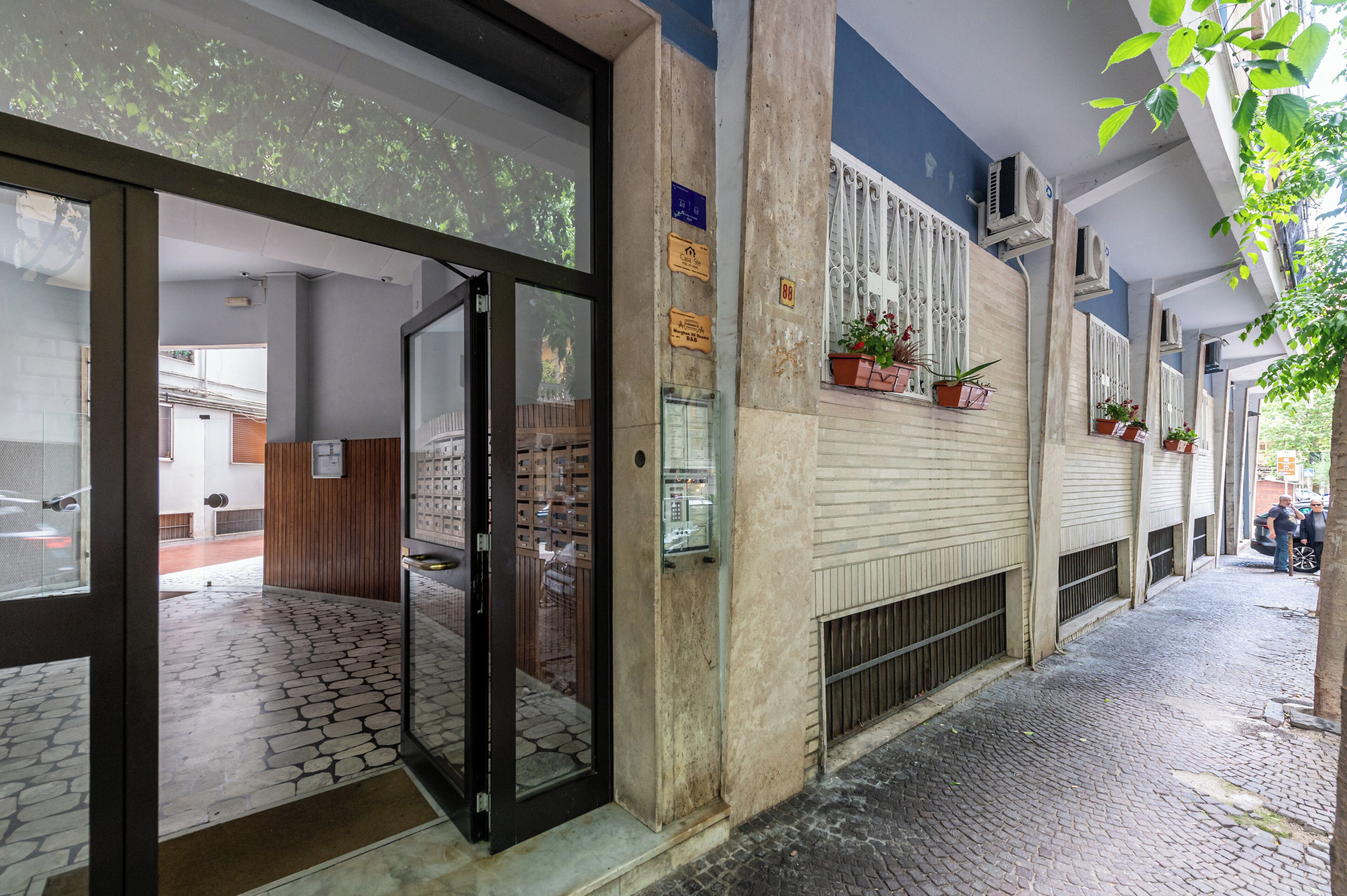 L'ingresso di un edificio con pavimento piastrellato, porta in vetro e parete con piante in vaso.