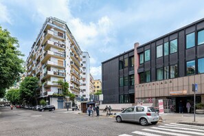 Un edificio a più piani con balconi, un complesso moderno con ampie finestre e un attraversamento pedonale con auto e pedoni.