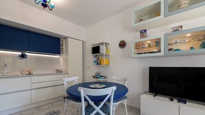 A modern kitchen with white cabinets, a blue dining table, and a flat-screen TV. - La Favola di San Martino (Naples)